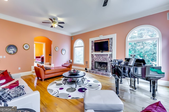 living room with a high end fireplace, light hardwood / wood-style flooring, ornamental molding, and ceiling fan