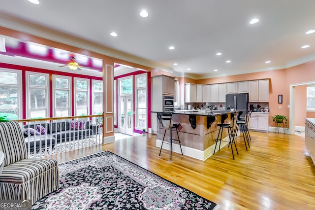 kitchen featuring an island with sink, light wood-type flooring, ceiling fan, black fridge, and a kitchen bar