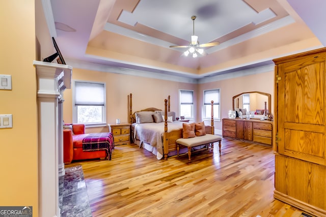 bedroom featuring ceiling fan, a tray ceiling, light wood-type flooring, and multiple windows