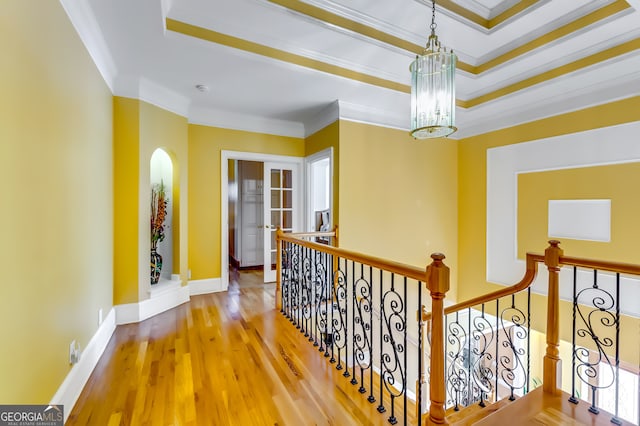 hallway with crown molding, a tray ceiling, hardwood / wood-style floors, and an inviting chandelier