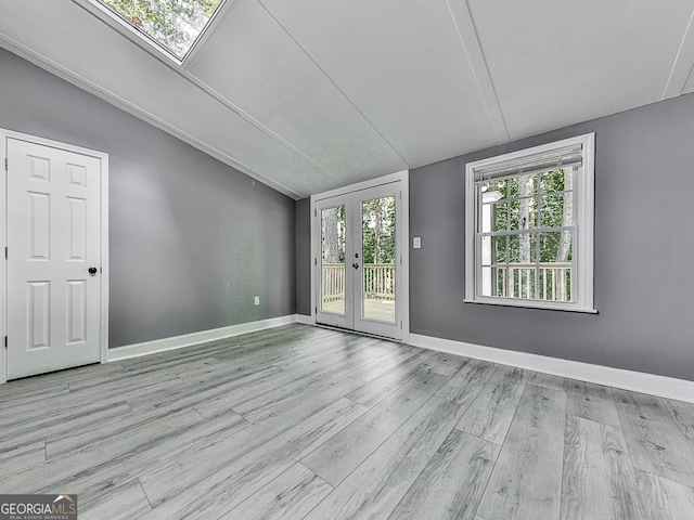 spare room featuring light wood-type flooring, vaulted ceiling, and french doors