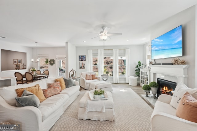 living room with a premium fireplace and ceiling fan with notable chandelier