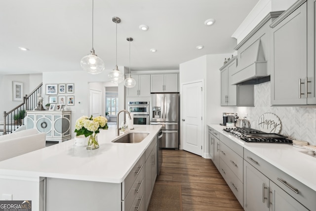 kitchen with a large island with sink, appliances with stainless steel finishes, sink, custom exhaust hood, and dark hardwood / wood-style floors