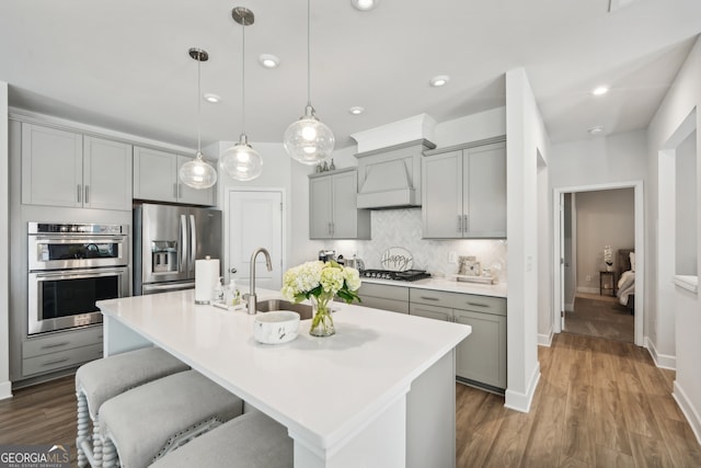 kitchen with dark hardwood / wood-style floors, stainless steel appliances, sink, decorative light fixtures, and custom exhaust hood