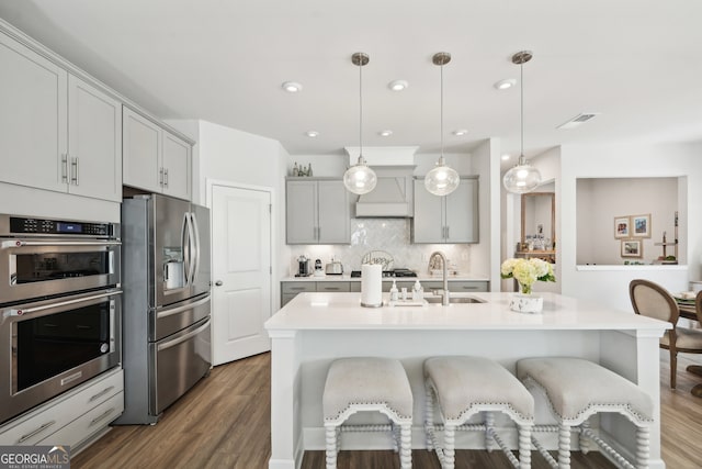 kitchen featuring a center island with sink, wood-type flooring, pendant lighting, gray cabinets, and stainless steel appliances