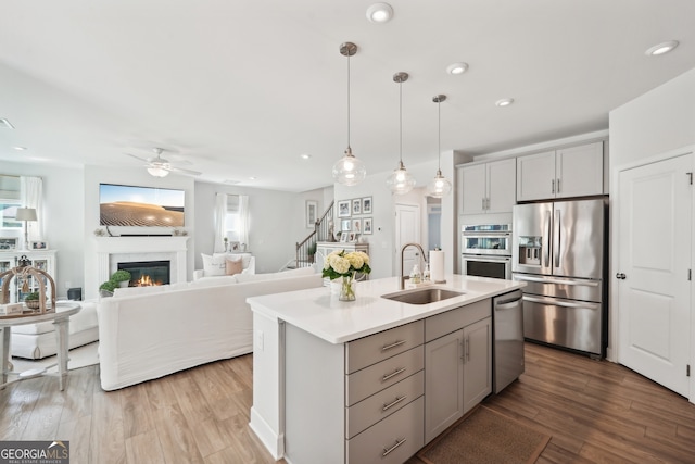 kitchen with a center island with sink, hanging light fixtures, sink, gray cabinetry, and stainless steel appliances