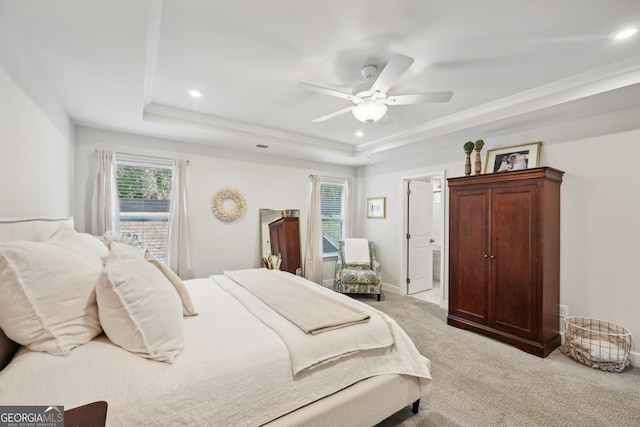 bedroom featuring connected bathroom, a raised ceiling, light carpet, and ceiling fan