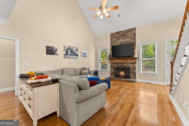 living room featuring ceiling fan, a stone fireplace, light hardwood / wood-style flooring, and high vaulted ceiling