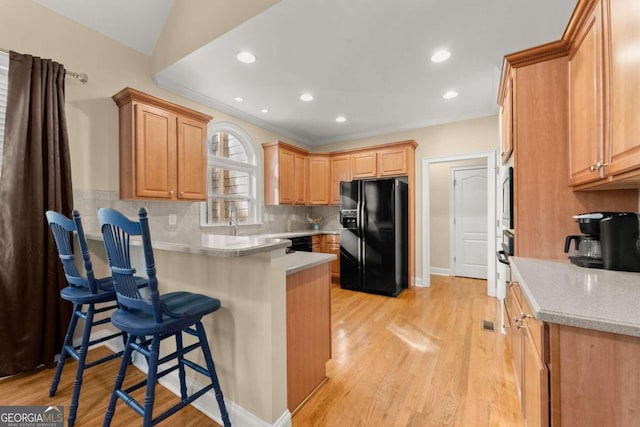 kitchen with lofted ceiling, decorative backsplash, black appliances, a breakfast bar area, and light wood-type flooring