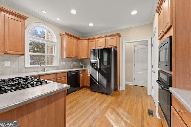 kitchen with light wood-type flooring, sink, black appliances, and decorative backsplash