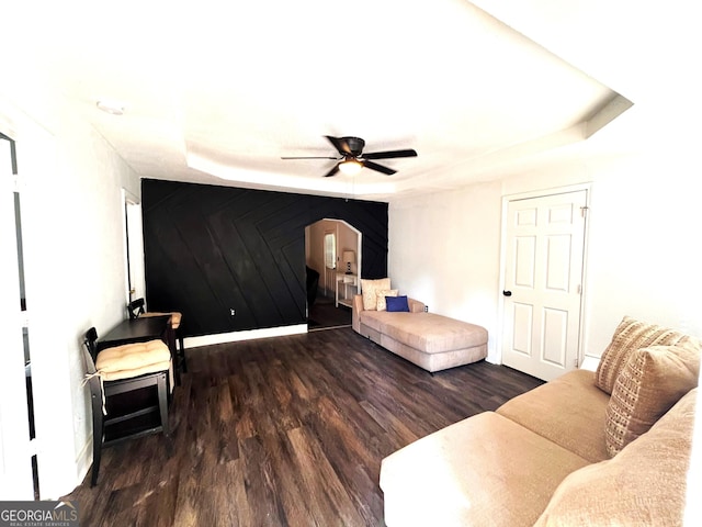 living room with a raised ceiling, ceiling fan, dark hardwood / wood-style flooring, and wooden walls