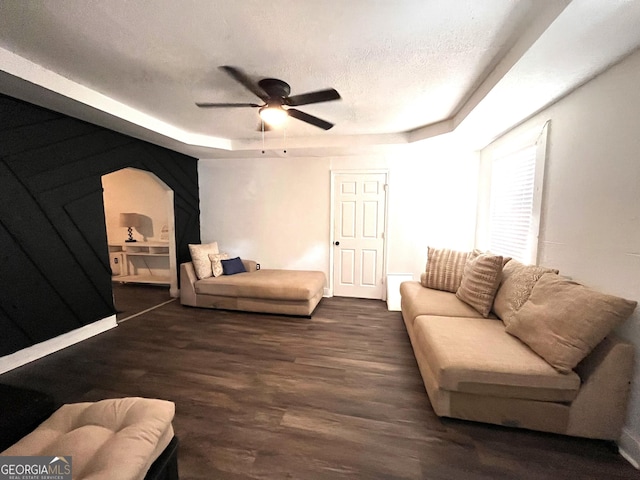 living room with a textured ceiling, ceiling fan, a raised ceiling, and dark wood-type flooring