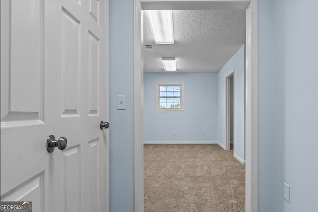 hallway featuring light colored carpet and a textured ceiling