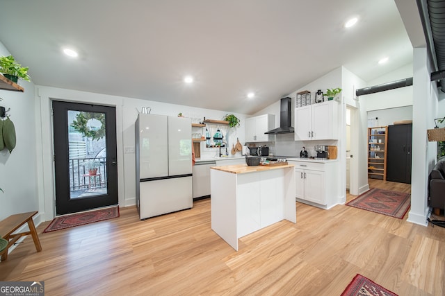 kitchen with wall chimney exhaust hood, a kitchen island, lofted ceiling, white cabinets, and white fridge