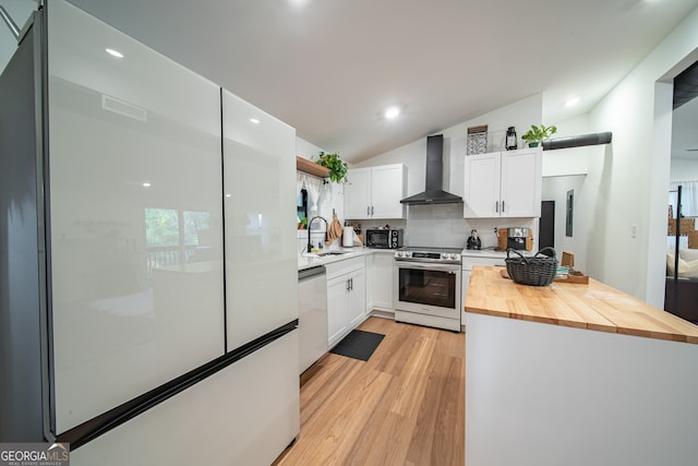 kitchen with wall chimney exhaust hood, wooden counters, vaulted ceiling, white cabinets, and appliances with stainless steel finishes