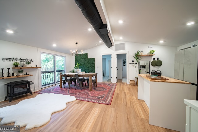 dining space with a wood stove, lofted ceiling, an inviting chandelier, and light wood-type flooring