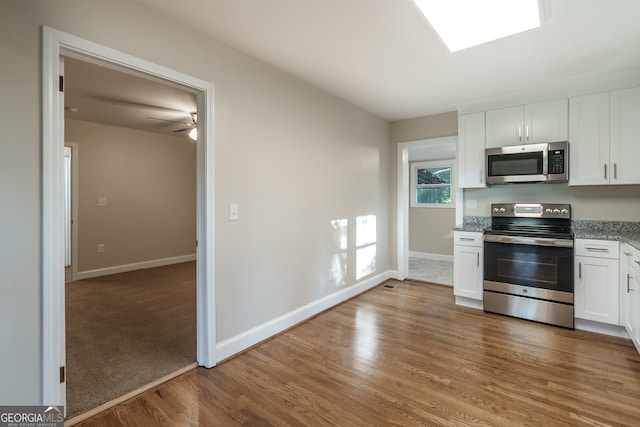 kitchen featuring wood-type flooring, light stone counters, stainless steel appliances, and white cabinets