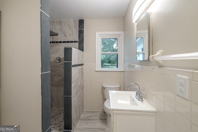 bathroom with vanity, tile walls, toilet, and tiled shower