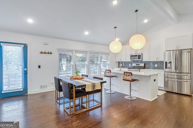 kitchen featuring a kitchen island, vaulted ceiling with beams, dark wood-type flooring, pendant lighting, and appliances with stainless steel finishes