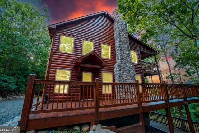 back house at dusk featuring a balcony and a wooden deck