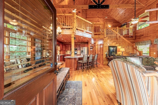 living room featuring beam ceiling, high vaulted ceiling, wooden ceiling, light hardwood / wood-style floors, and wood walls