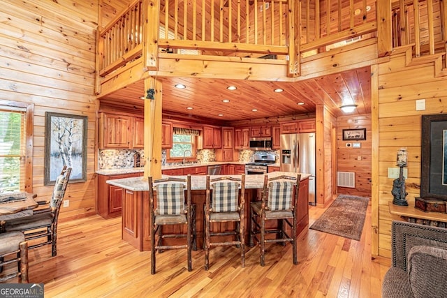 kitchen with a wealth of natural light, wooden walls, stainless steel appliances, and light wood-type flooring