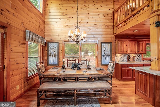 dining space with a high ceiling, light wood-type flooring, wooden walls, and a notable chandelier