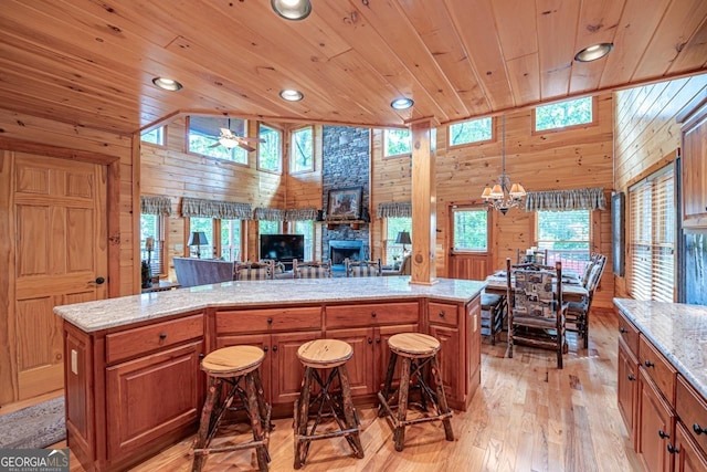 kitchen with a center island, light hardwood / wood-style floors, a kitchen bar, wooden walls, and ceiling fan with notable chandelier