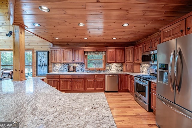 kitchen with stainless steel appliances, light hardwood / wood-style flooring, plenty of natural light, and wooden walls