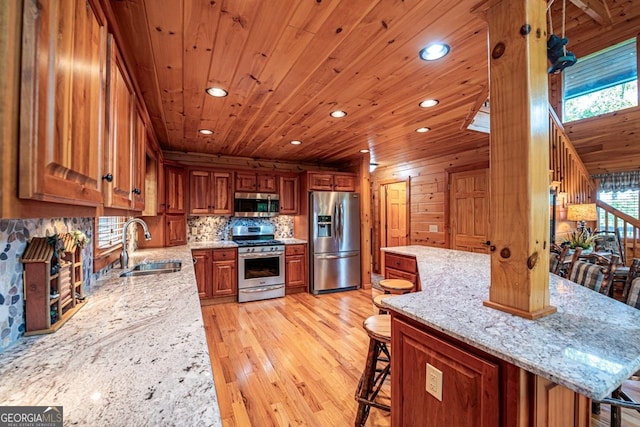 kitchen featuring light wood-type flooring, stainless steel appliances, sink, a breakfast bar area, and wood walls