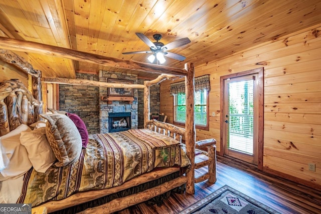 bedroom with wood walls, a stone fireplace, beamed ceiling, wood-type flooring, and wood ceiling