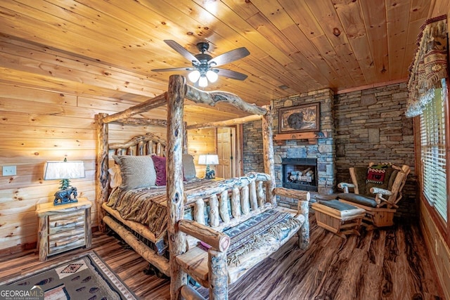 bedroom with wood walls, wooden ceiling, ceiling fan, a fireplace, and wood-type flooring