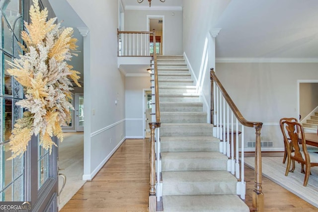 staircase featuring wood-type flooring, crown molding, and a chandelier