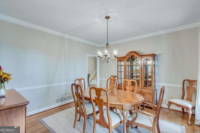 dining room featuring light hardwood / wood-style floors, crown molding, and a notable chandelier