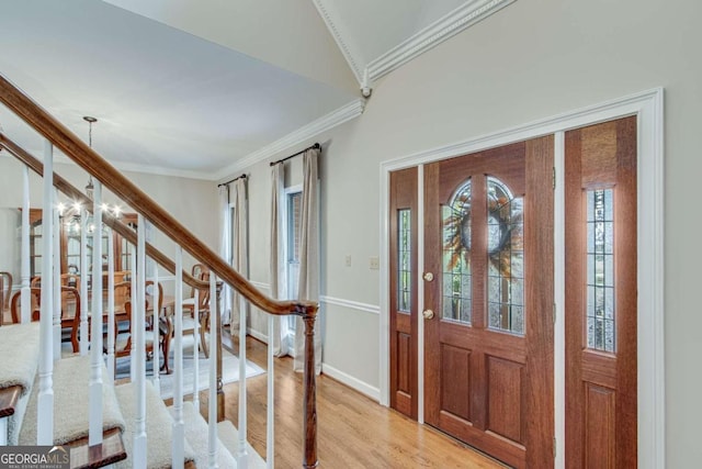 entrance foyer with ornamental molding, lofted ceiling, an inviting chandelier, and light hardwood / wood-style floors