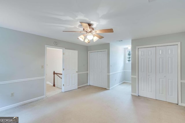 unfurnished bedroom with light carpet, ceiling fan, and multiple closets