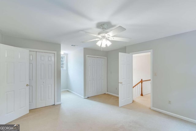 unfurnished bedroom with light carpet, ceiling fan, and two closets