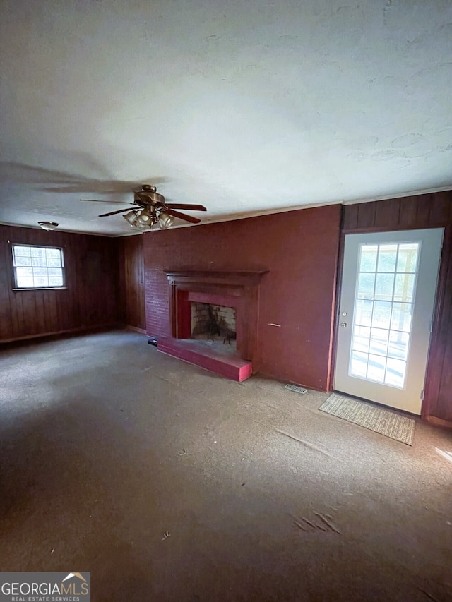 unfurnished living room with wood walls, light colored carpet, and ceiling fan