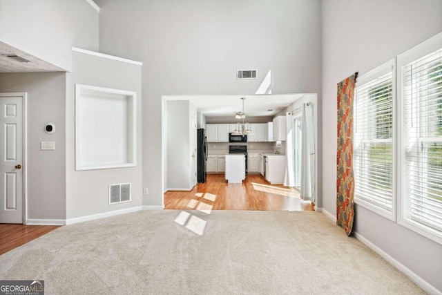 unfurnished living room featuring a high ceiling, sink, and light hardwood / wood-style floors