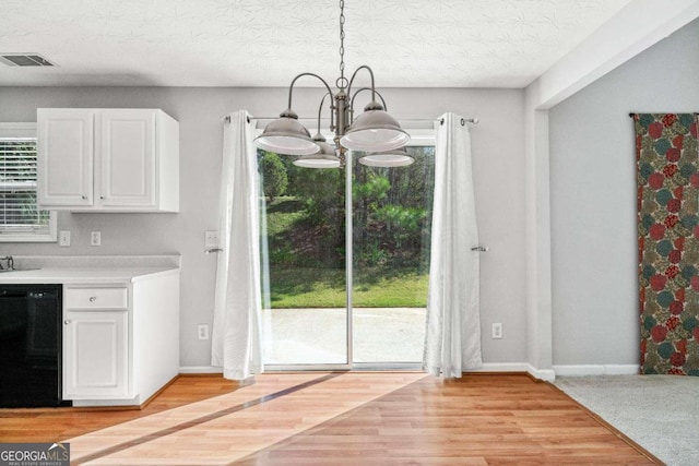 unfurnished dining area with plenty of natural light, an inviting chandelier, light hardwood / wood-style floors, and a textured ceiling