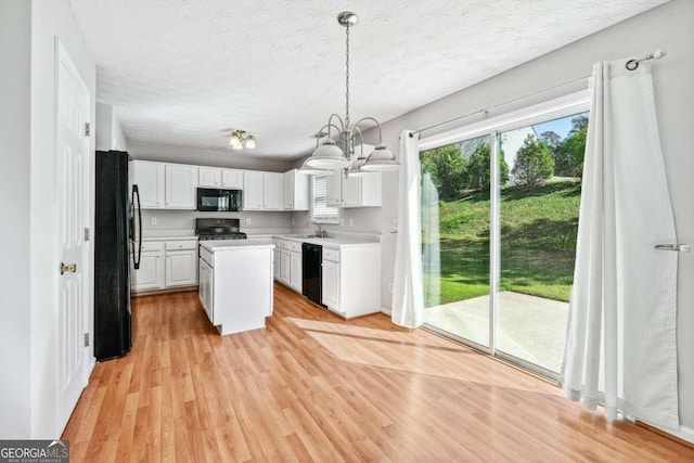 kitchen with black appliances, sink, white cabinetry, light hardwood / wood-style flooring, and decorative light fixtures