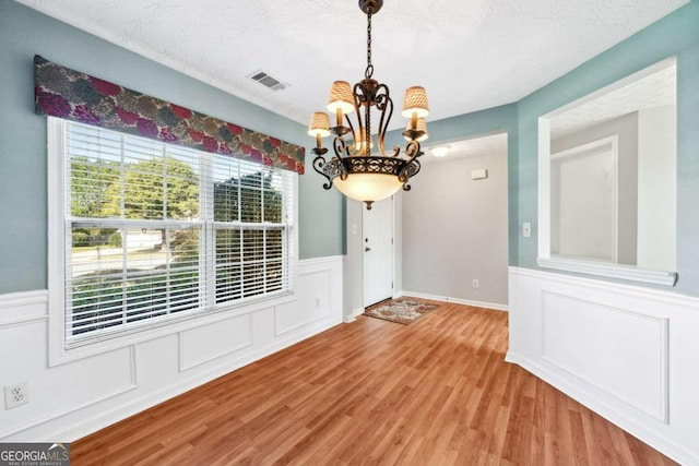 unfurnished dining area with a notable chandelier, wood-type flooring, and a textured ceiling