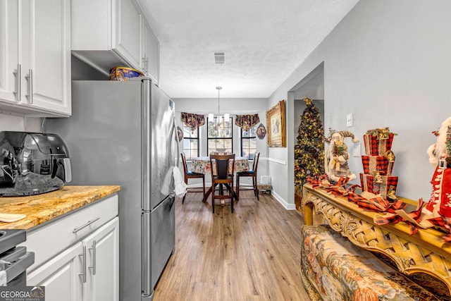 kitchen with light stone countertops, light wood-type flooring, white cabinets, a chandelier, and hanging light fixtures