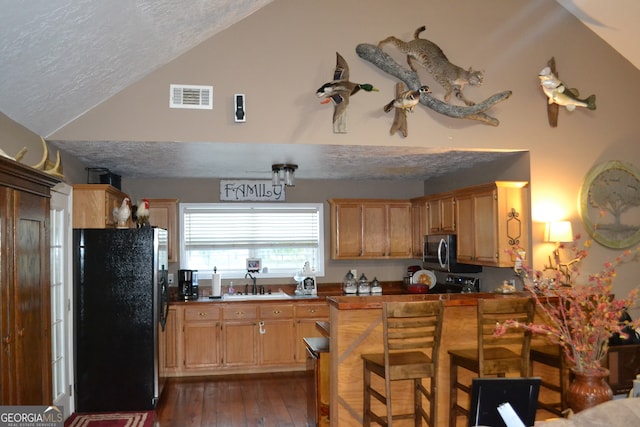 kitchen featuring black fridge, a textured ceiling, dark hardwood / wood-style floors, and vaulted ceiling