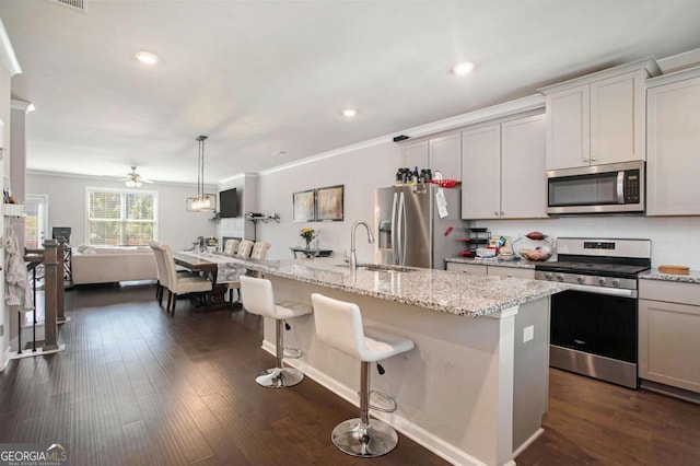 kitchen with an island with sink, dark hardwood / wood-style floors, sink, appliances with stainless steel finishes, and decorative light fixtures