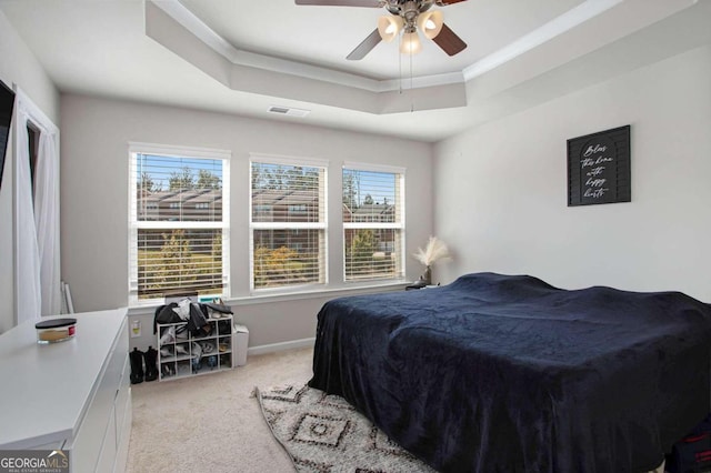 carpeted bedroom with ceiling fan, a tray ceiling, and multiple windows