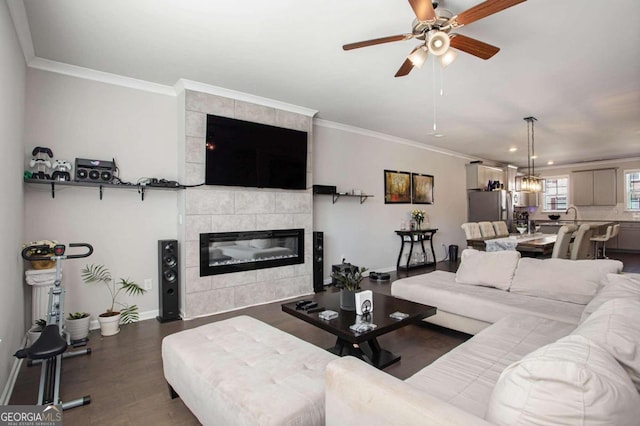 living room featuring wood-type flooring, ornamental molding, a tile fireplace, and ceiling fan