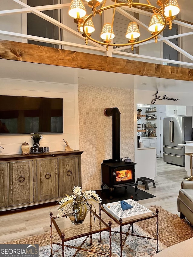 living room with an inviting chandelier, high vaulted ceiling, light hardwood / wood-style flooring, a wood stove, and beam ceiling