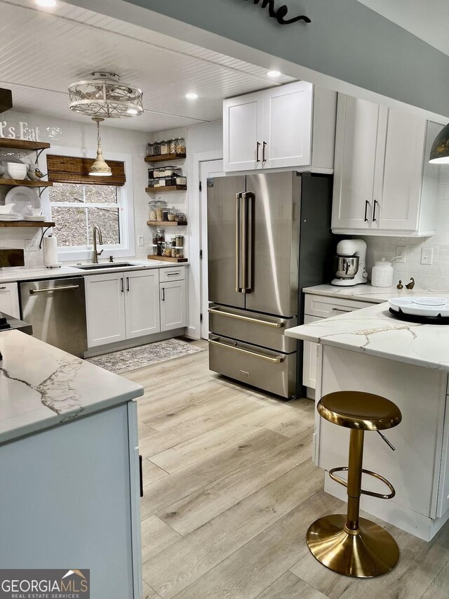 kitchen featuring stainless steel appliances, sink, white cabinets, and decorative light fixtures