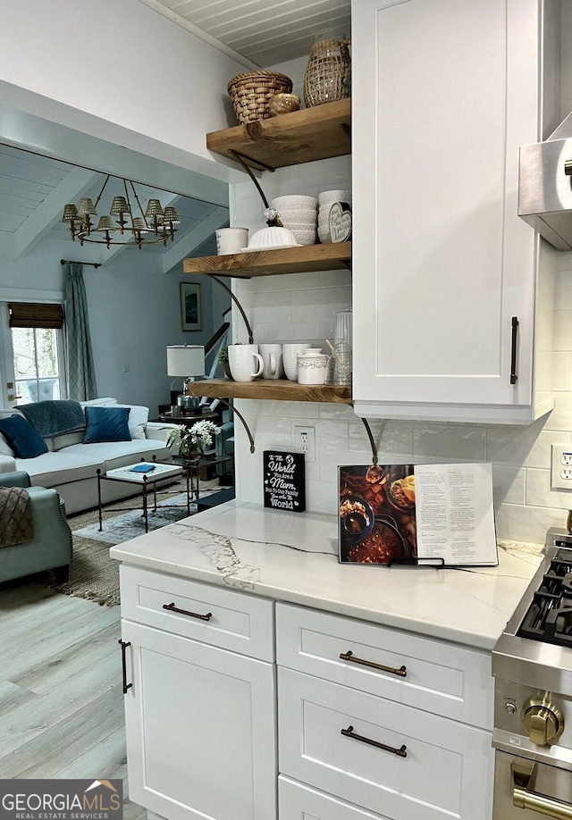 kitchen featuring white cabinetry, stainless steel gas range oven, light stone counters, and decorative backsplash